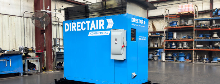 A large blue commercial DIRECTAIR machine in an industrial workshop with equipment and metal parts on shelves in the background.