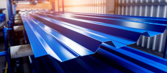 Stack of corrugated blue steel sheets with a glossy finish on an industrial conveyor belt.